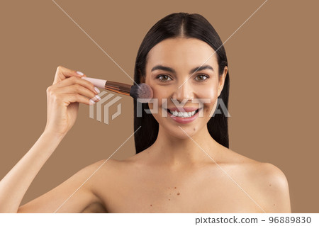 Headshot of youngsmiling beautiful woman holding makeup brush, applying blush 96889830