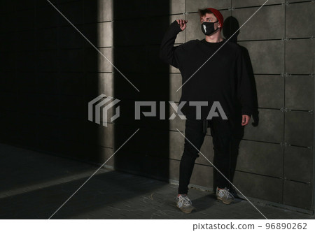 Portrait of a young man standing in a black t-shirt and black medical mask and red cap to protect against virus, covid-19 outbreak. 96890262