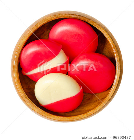 Snack cheese disks in red wax encasements, in a wooden bowl. Small edam slices, each one encased in a blend of red colored paraffin and microcrystalline wax. Two disks with partly removed encasements. 96890487