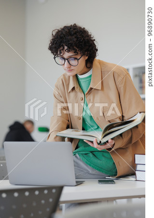 confident woman in library or coworking works laptop online, female student reads book 96890730