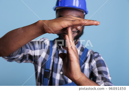 Smiling builder making the gesture of waiting time and pause in the studio, expressing the t-shape sign with his hands to pause the work. African american construction worker gesturing rejection and Smiling builder making the gesture of waiting time and pause in the studio, expressing the t-shape sign with his hands to pause the work. African american construction worker gesturing rejection and 96891850