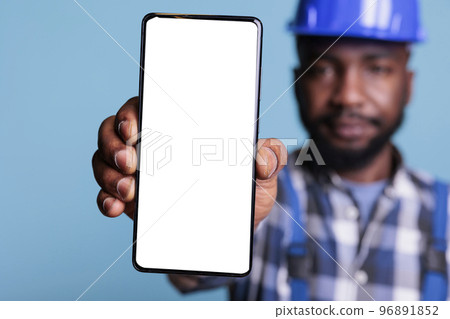 Professional man holding smartphone with white screen display in studio, using work uniform and protection helmet. Having mobile phone with blank copy space, construction industry concept. 96891852
