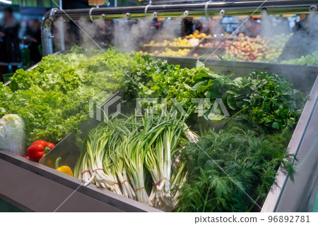 Sale of fresh green vegetables - lettuce salad, parsley, dill, green onions, herbs. Fresh herbs on display at grocery store under cooling water steam. Vegetables sprayed with mist water from nozzles Sale of fresh green vegetables - lettuce salad, parsley, dill, green onions, herbs. Fresh herbs on display at grocery store under cooling water steam. Vegetables sprayed with mist water from nozzles 96892781