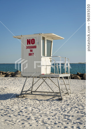 Small white lifeguard tower on a beach shore with rocks near the water at Destin, Florida 96893030