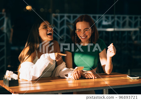 Girls using smartphones while sitting and pointing finger Girls using smartphones while sitting and pointing finger 96893721