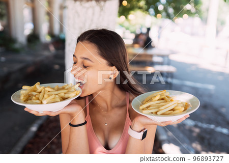 Young women hold french fries on white plates. Street cafe Young women hold french fries on white plates. Street cafe 96893727