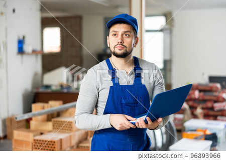 Portrait of a builder, standing holding a laptop Portrait of a builder, standing holding a laptop 96893966