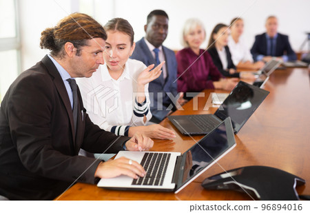 Mid-aged white businessman co-working on laptop with his young female colleague at office Mid-aged white businessman co-working on laptop with his young female colleague at office 96894016