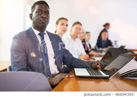 Mature african businessman sitting at meeting and listening to colleague's report Mature african businessman sitting at meeting and listening to colleague's report 96894305
