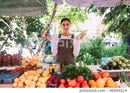 Young saleswoman holding zucchini and tomato in hands 96894824