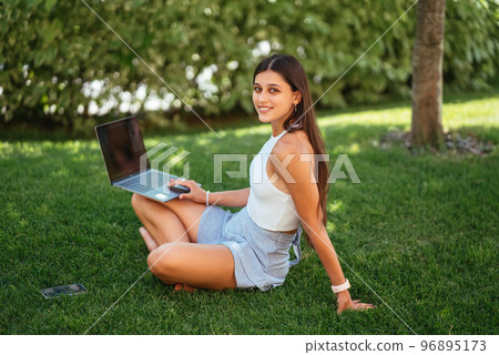 Young girl works with a laptop, sitting on the lawn. 96895173