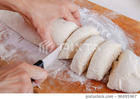 Female hands cut with a knife a kneaded dough on a wooden board. Homemade cooking.  Female hands cut with a knife a kneaded dough on a wooden board. Homemade cooking.  96895967