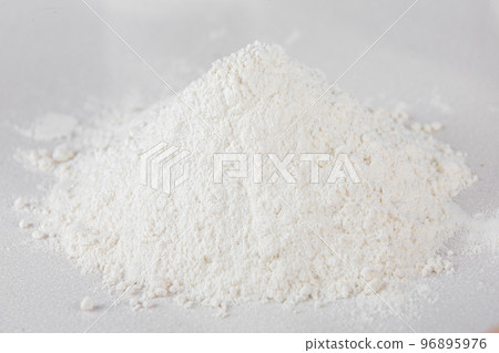 A handful of sifted white flour on a white tabletop background. Scattered flour. A handful of sifted white flour on a white tabletop background. Scattered flour. 96895976