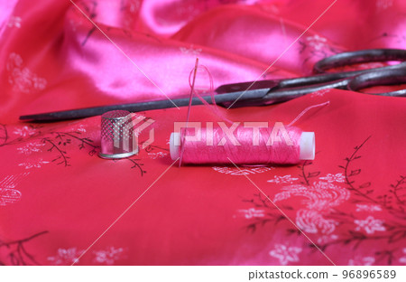 Spool of Pink Thread and Thimble on Vintage Pink Satin Fabric 96896589