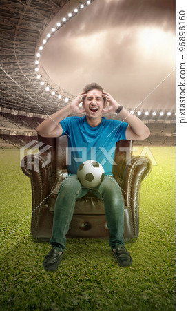 Asian man with the ball sitting on the couch with a disappointed expression Asian man with the ball sitting on the couch with a disappointed expression 96898160