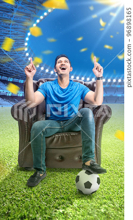 Asian man with the ball sitting on the couch with an excited expression 96898165