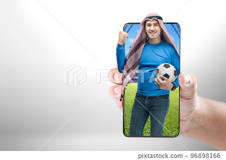 Asian man with keffiyeh standing while holding the ball with an excited expression on the football stadium 96898166