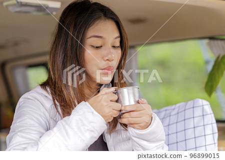 Asian woman holding a hot drink inside the campervan enjoying camp activity Asian woman holding a hot drink inside the campervan enjoying camp activity 96899015