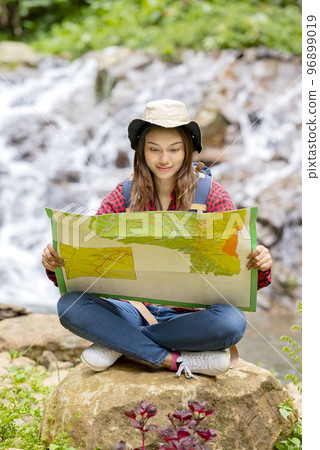 Asian woman in a hat and backpack holding maps 96899019