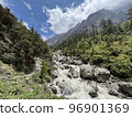 A raging and wild river flows between rocks in the valley with mountains beside it under a blue sky Langtang Trek Trail at Lantan in Nepal 96901369
