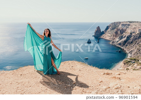 Side view a Young beautiful sensual woman with black hair in a long mint dress posing on a beach with calm sea bokeh lights on sunny day. Girl on the nature on blue sky background. Fashion photo 96901594