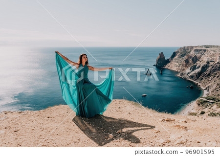 Side view a Young beautiful sensual woman with black hair in a long mint dress posing on a beach with calm sea bokeh lights on sunny day. Girl on the nature on blue sky background. Fashion photo 96901595