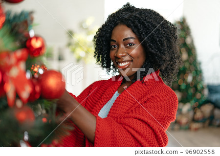 Beautiful young african woman decorating Christmas tree at home Beautiful young african woman decorating Christmas tree at home 96902558