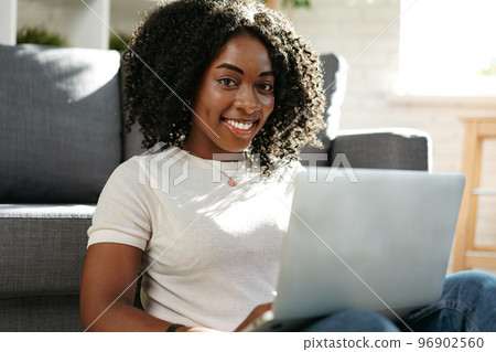 Beautiful african woman working with laptop at home in living room Beautiful african woman working with laptop at home in living room 96902560