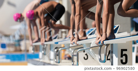 Teenage children on the starting blocks ready to dive into the pool at the beginning of a swimming race Teenage children on the starting blocks ready to dive into the pool at the beginning of a swimming race 96902580