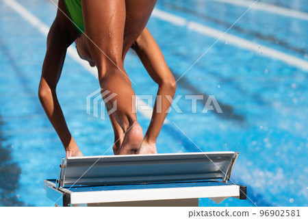 Swimmer in low position on starting block in a swimming pool 96902581