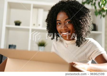 Young african woman sit on couch at home unpacking parcel cardboard box with online purchase Young african woman sit on couch at home unpacking parcel cardboard box with online purchase 96902599