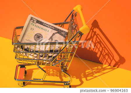 US dollar paper currency 5 banknote money Shopping trolley cart on colorful orange yellow background. Copy space for your text. Online shopping, buy mall market shop consumer concept. Small toy 96904163