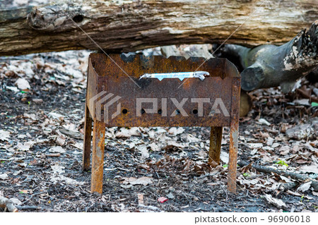 A rusted disposable barbecue grill thrown near a fire in nature A rusted disposable barbecue grill thrown near a fire in nature 96906018