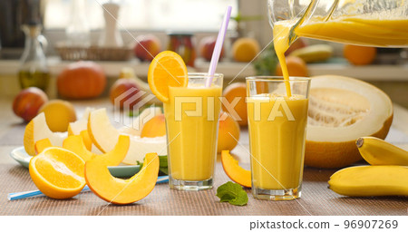 Melon banana orange Smoothie is poured into a glass on the background of fresh fruits Melon banana orange Smoothie is poured into a glass on the background of fresh fruits 96907269