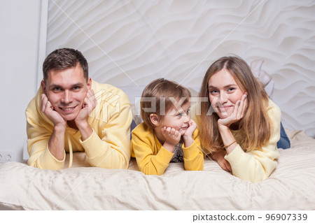 Portrait of lovely family, parents, mom and dad with adorable child son on the bed Portrait of lovely family, parents, mom and dad with adorable child son on the bed 96907339