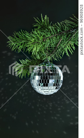 Christmas decoration in the form of a disco ball hanging on a spruce branch on a dark background 96908928