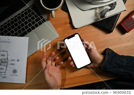 Above view of engineer man hands holding smart phone over his workstation. Blank screen for your advertise 96909838