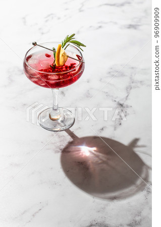 Pomegranate Christmas iced cocktail with rosemary and lemon on white marble background isolated with clear shadows in hard light, space for text. Xmas drink 96909909
