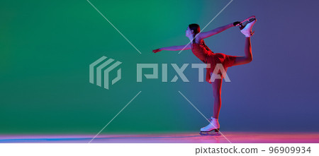 Young sportive girl, junior female figure skater in red stage costume skating isolated over gradient green-blue background in neon light. Grace, beauty, winter sports Young sportive girl, junior female figure skater in red stage costume skating isolated over gradient green-blue background in neon light. Grace, beauty, winter sports 96909934