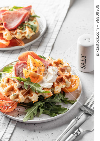 Cheese or potato savory waffles served with with tomatoes, ham and aragula with cutlery. Delisious savory breakfast 96909939