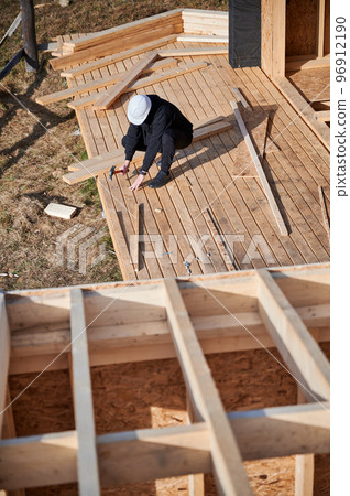 Man worker building wooden frame house. Carpenter hammering nail into wooden board, using hammer. Carpentry concept. 96912190