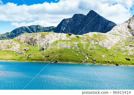 Climbing up mount Snowdon in North Wales. View of the hills and mountains, green grass and beautiful blue lakes on the way to the top. Climbing up mount Snowdon in North Wales. View of the hills and mountains, green grass and beautiful blue lakes on the way to the top. 96913414