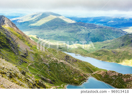 Climbing up mount Snowdon in North Wales. View of the hills and mountains, green grass and beautiful blue lakes on the way to the top. 96913418