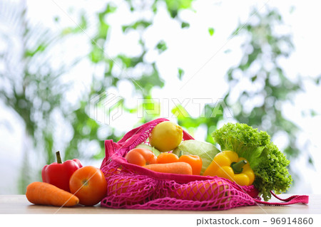 Net bag with vegetables on table against blurred background Net bag with vegetables on table against blurred background 96914860