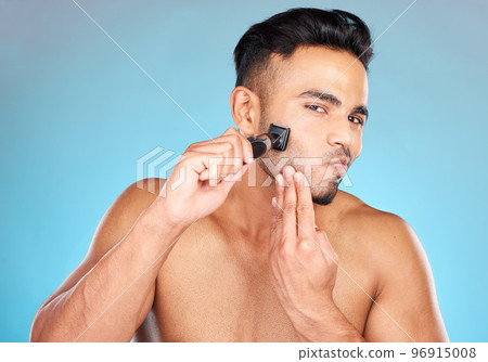 Man, shave and razor for wellness, skincare and cosmetics against blue studio background. Indian male, beard and shaver for natural beauty, smooth and clear skin for treatment, routine and grooming. Man, shave and razor for wellness, skincare and cosmetics against blue studio background. Indian male, beard and shaver for natural beauty, smooth and clear skin for treatment, routine and grooming. 96915008