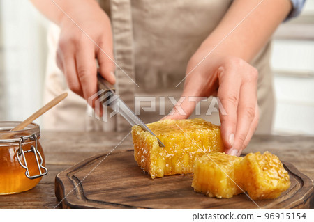 Woman cutting fresh honeycomb at table, closeup 96915154