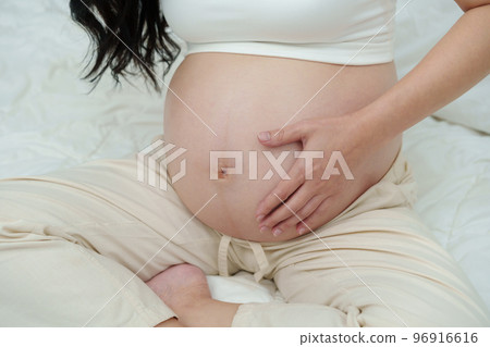 close up pregnant woman stroking her belly on bed 96916616