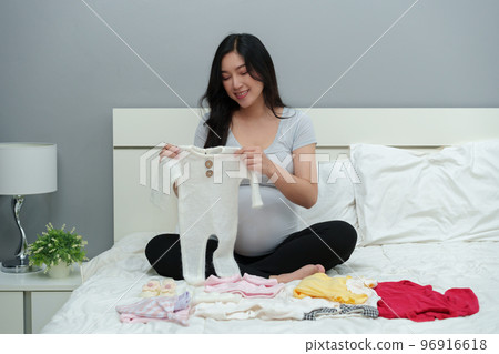 pregnant woman packing baby clothes for newborn on bed 96916618