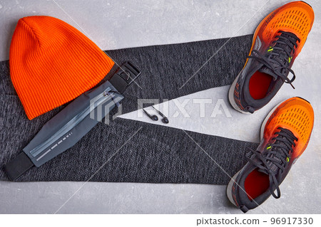 An orange knitted warm hat, warm sports leggings, a fanny pack with headphones and orange sneakers on a light concrete background 96917330