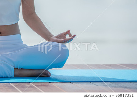 Woman in white yoga suit sitting meditating in the morning at lake. Woman in white yoga suit sitting meditating in the morning at lake. 96917351